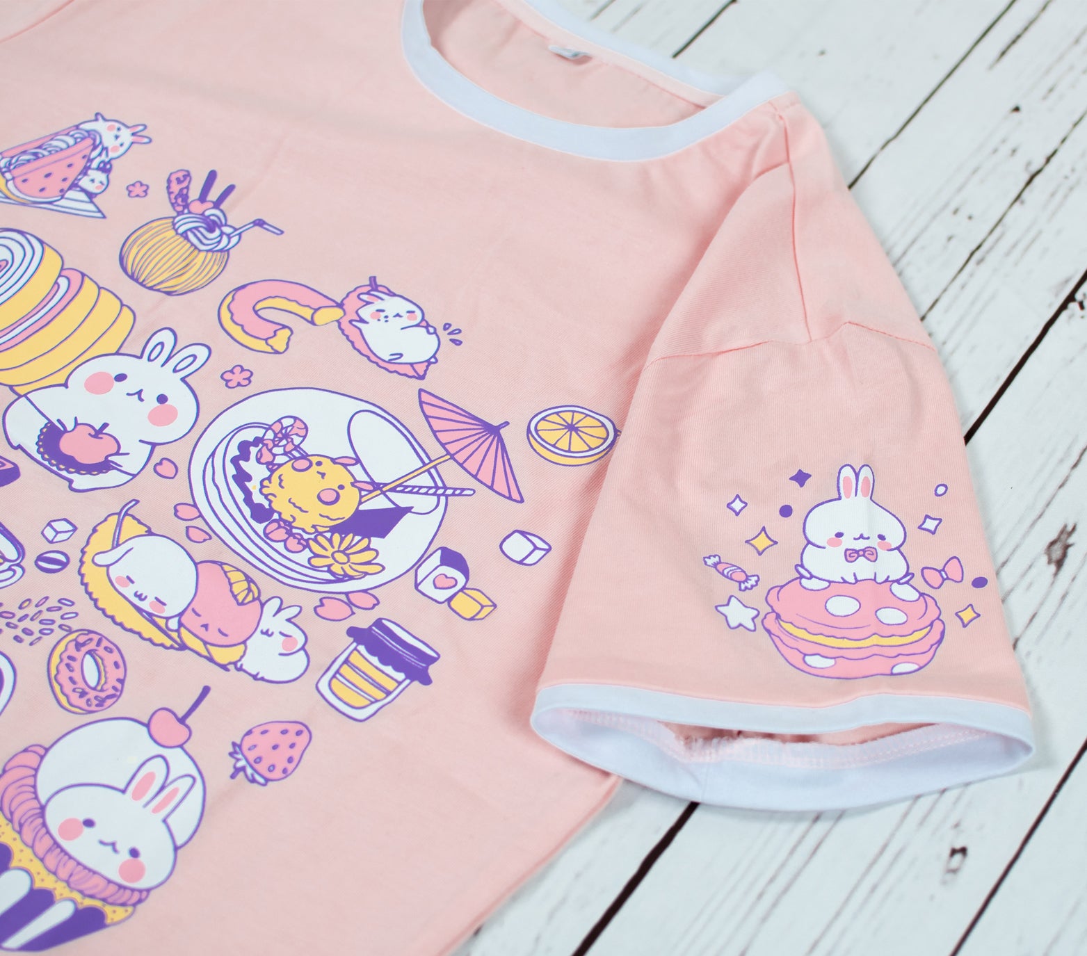 Light peach pink bunny t-shirt showing sweet bunny chefs making baking and café goods such as sweets, drinks, and desserts. The left sleeve of the shirt also shows a bunny sitting on a pink macraon. Light-weight and stretchable material that is made of 100% cotton. The collar and sleeve ends have cute white borders that truly frames the look of this summer shirt. Available in sizes XXS to 2XL.  