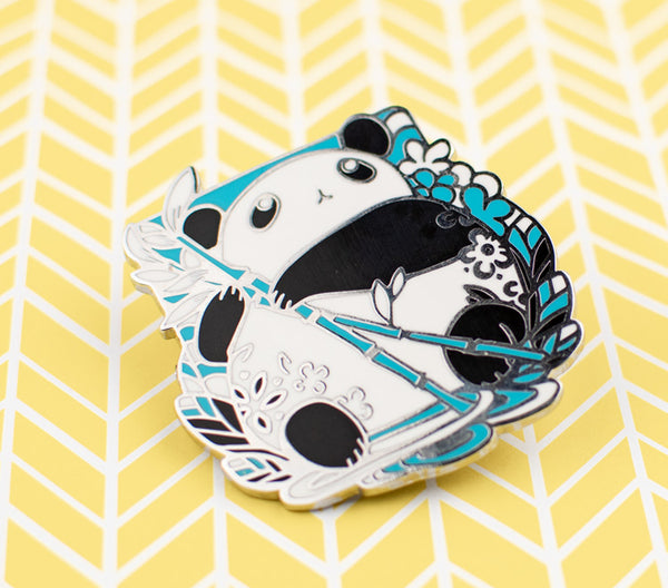The pin design features a chibi panda holding a bamboo stem and looking up. The pin is printed on silver metal and has two rubber back pins in place for you to attach the pin to your clothes, bags, etc.  