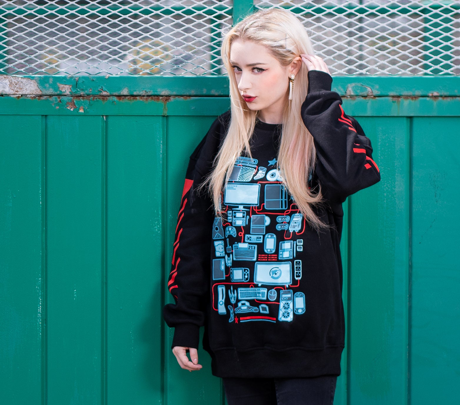 Black sweatshirt with front screen printed design of various console gaming consoles and controllers illustrated in cyan. The front shirt design also features PC gaming as well as mobile gaming devices. The sleeves features slanted red stripes that gives the shirt a streetwear feel. The sweatshirt comes in black with an ultra-soft exterior jersey fabric and a fuzzy soft interior. Sweatshirt comes in XS to 2XL
