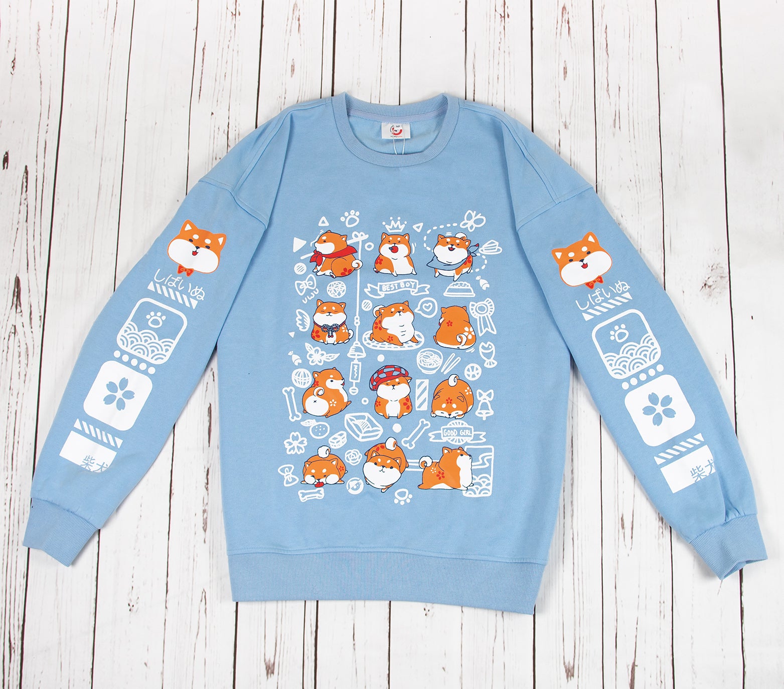 This light blue sweatshirt features a front design of a group of shiba inu in various adorable poses. The design captures the various antics of the shiba inu. Both sleeves also feature designs that run down the sleeves, which matches the front main design of the sweatshirt. The material is medium heavy jersey style with a soft fleece interior. The sweatshirt comes in sizes from XXS to 2XL. 